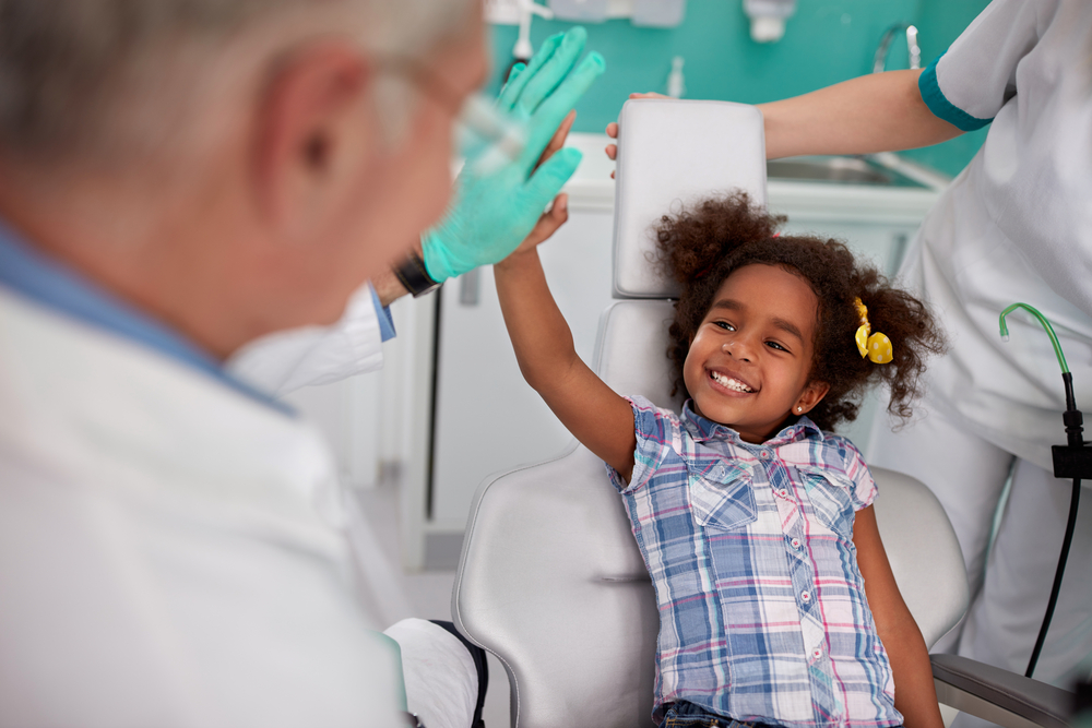 Little girl with a plaid shirt and hairbow high fiving her orthodontist.