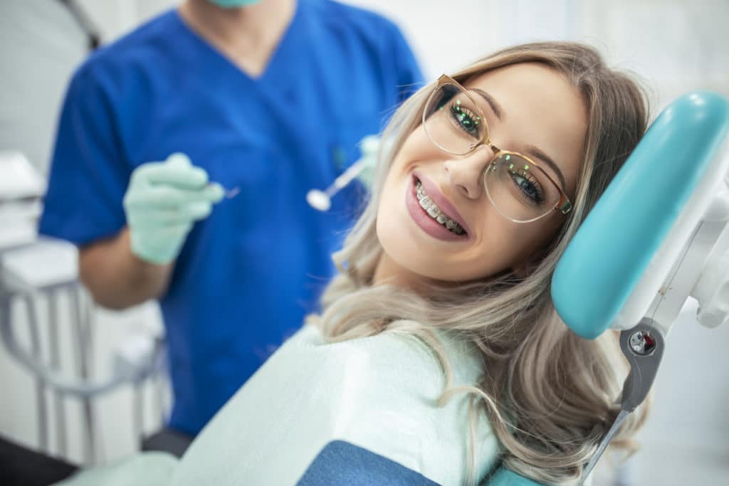 a woman with braces and glasses getting her braces inspected by the dental assistant