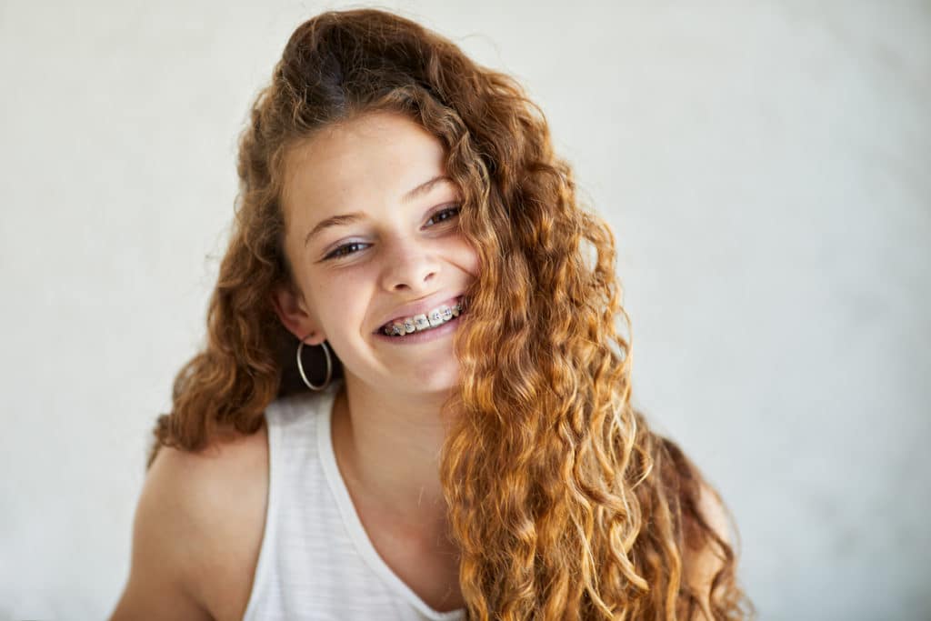 a girl with very curly hair smiling with her traditional metal braces