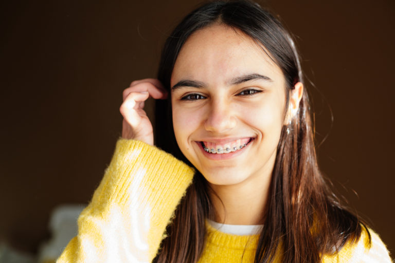 a teenage girl with a yellow sweater smiling to show off her metal braces