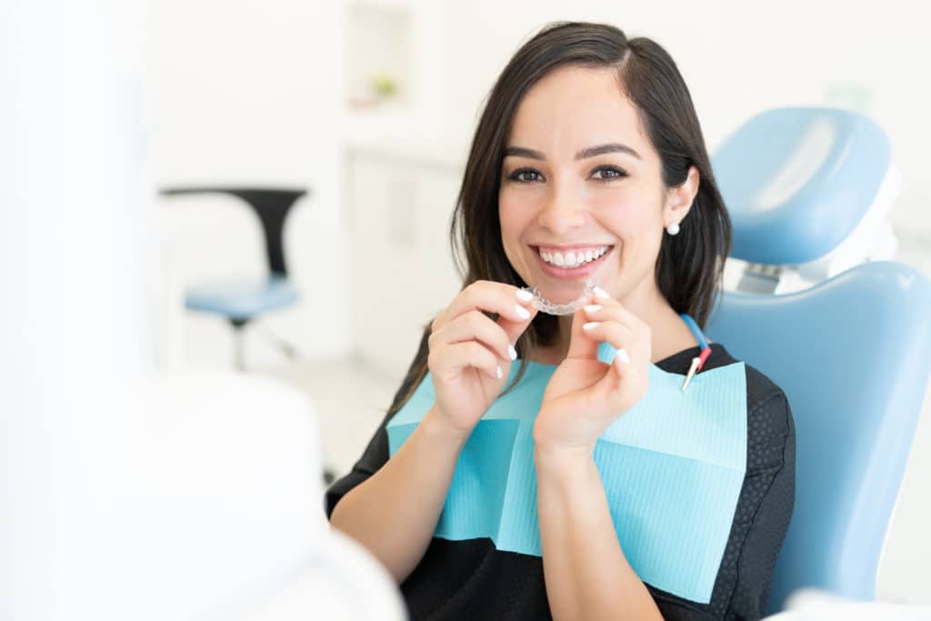 an orthodontist patient holding her invisalign clear aligners while sitting on the dental chair