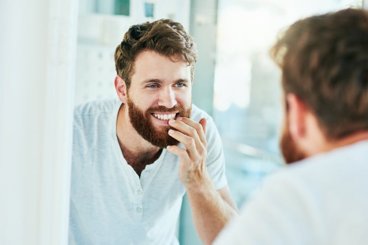 a man with a beard inspecting his teeth in the mirror