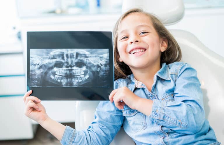 a child sitting on the dental chair holding up an xray of her teeth