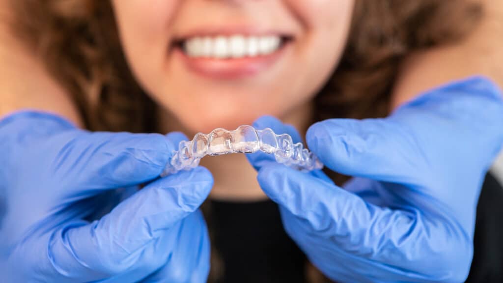 Dr. Vinson in gloves applying invisible aligner on female patient teeth at the Wake Forest location.
