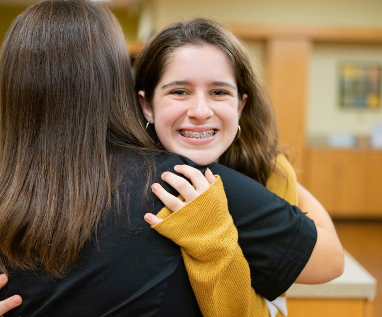 Teen with braces in Wake Forest, NC smiling and hugging her favorite orthodontist assistant