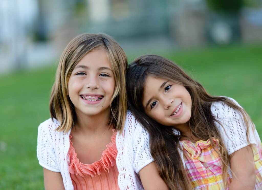 Adorable happy girls sitting side by side. One is resting her head on the other's shoulder.