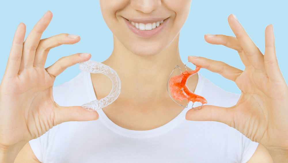 Woman holding up a clear retainer in one hand and a metal retainer in the other