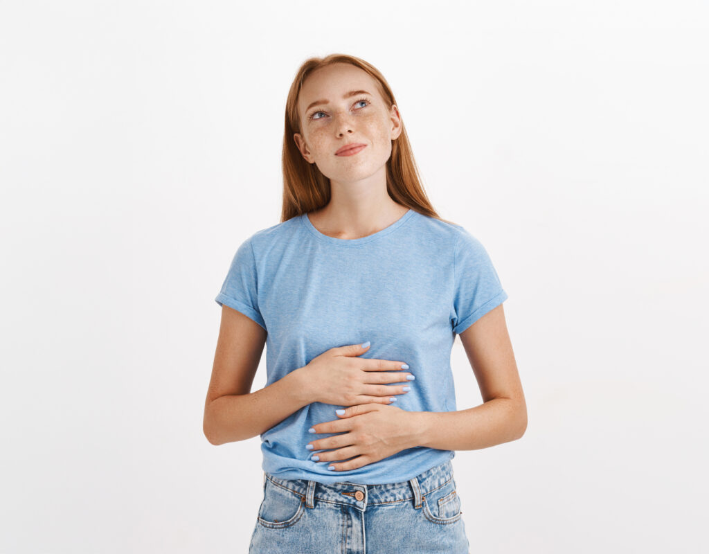 Woman Remembering Tasty Food She Ate In New Restaurant Rubbing Tummy Or Belly Looking At Upper Left Corner Nostalgic And Happy Liking Eat Delicious Meals Standing In Blue T Shirt Over Gray Background
